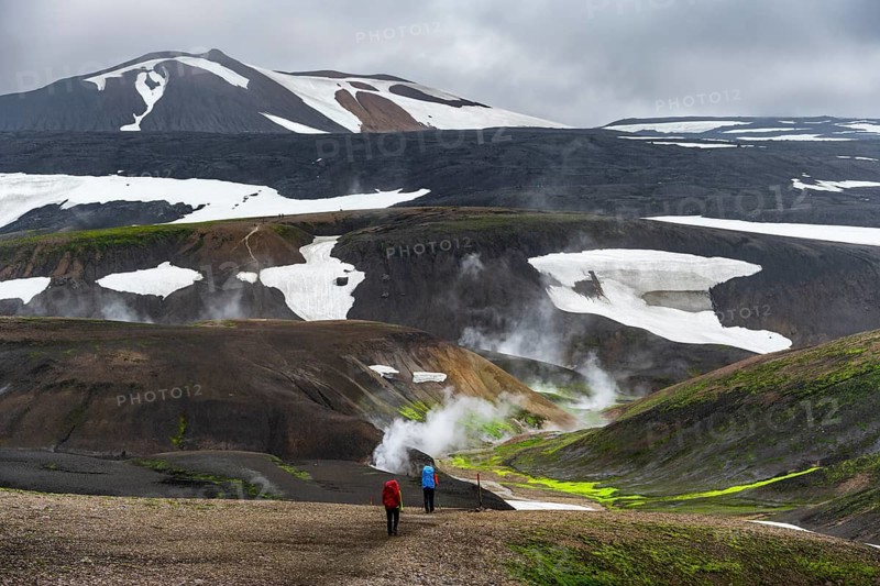Hikers in dramatic volcanic landscape with mountains and snow, volcanic steaming hot springs, trekking trail Laugavegur, Landmannalaugar, Fjallabak Nature Reserve, Icelandic Highlands, Suðurland, Iceland