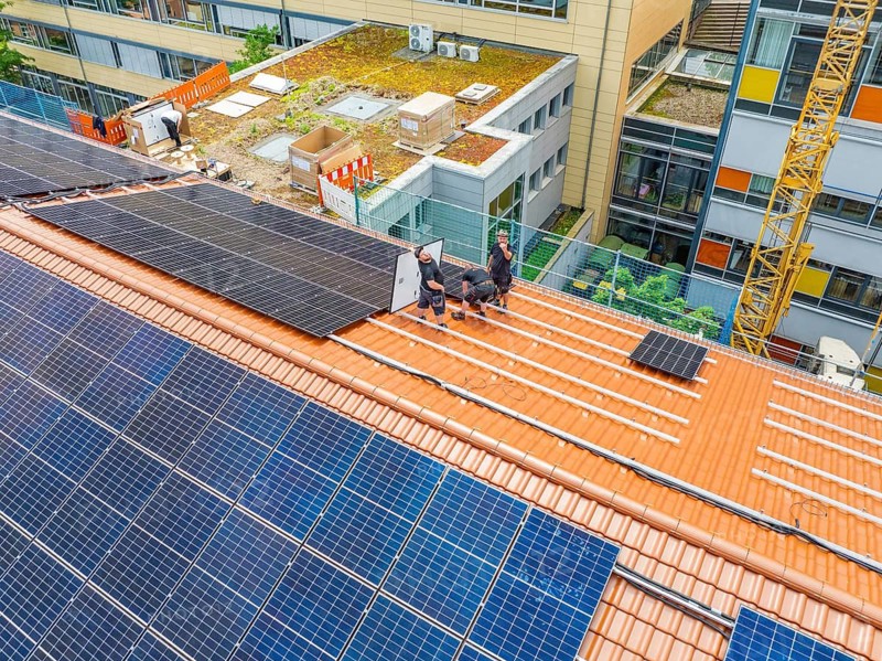 Assembly of solar modules by workers on urban roof, new PV system at Heinrich-Immanuel-Perrot secondary school, city of Calw, Germany