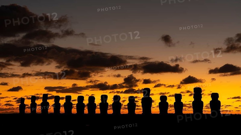 Moai statues in silhouette against orange morning sky with clouds, Ahu Tongariki, Easter Island, Chile