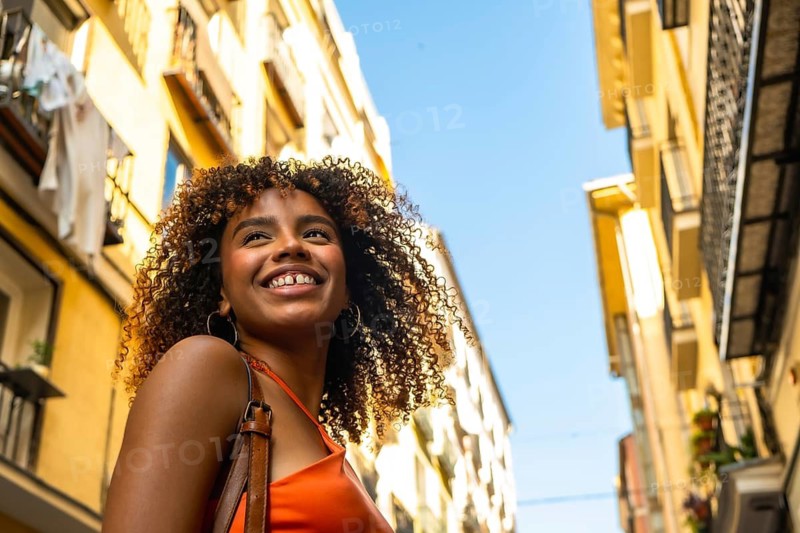 Young black woman with curly hair exploring a city, enjoying travel and urban life, smiling with happiness and optimism under a blue sky between historical buildings