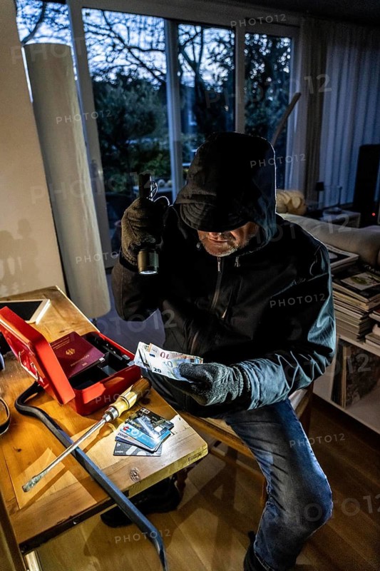 Symbolic image of a burglary, perpetrator has broken into a flat from the garden side and is looking for loot, breaks open a cash box, finds valuables, money