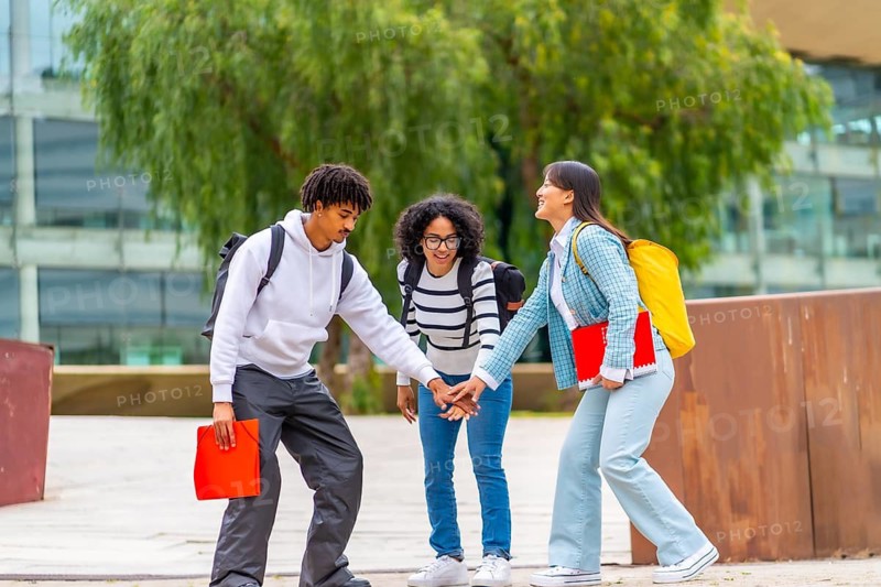 Full length photo of three multi-ethnic students stacking hands to celebrate unity in the campus