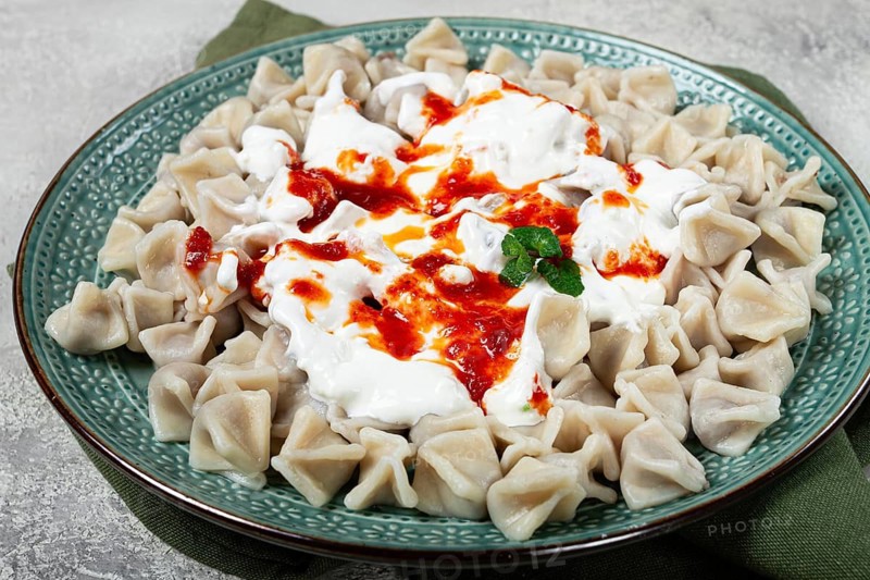 The dish features a generous serving of Turkish dumplings topped with velvety yogurt and a drizzle of spicy red sauce, displayed on a beautifully crafted plate with a green accent