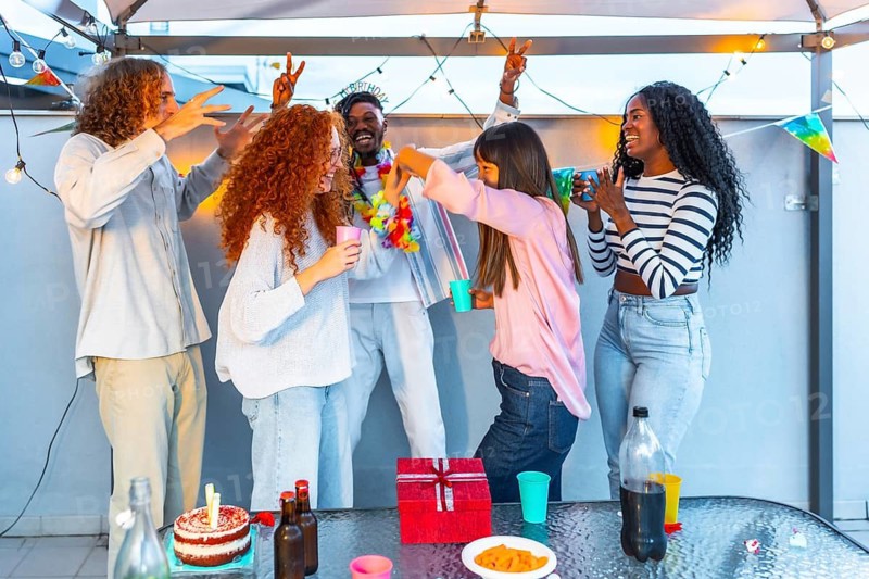 Happy multiracial group of friends dancing celebrating birthday party at terrace