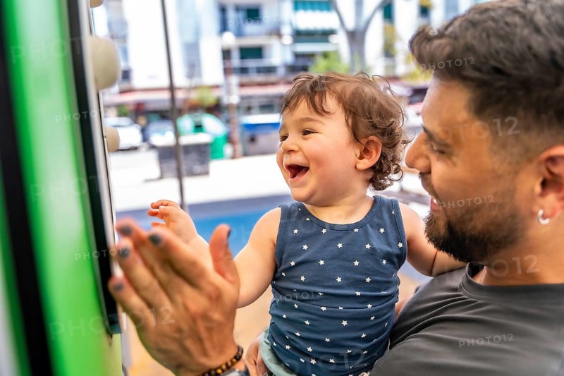 Father holding his adorable baby son while playing enthusiastically at a playground, with the child laughing joyfully and interacting with a colorful toy, showcasing their strong familial bond