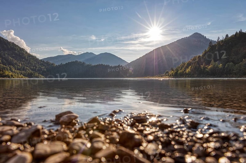 Peaceful lake with mountain backdrop, golden sky and sunlight on water and stones, Weitsee