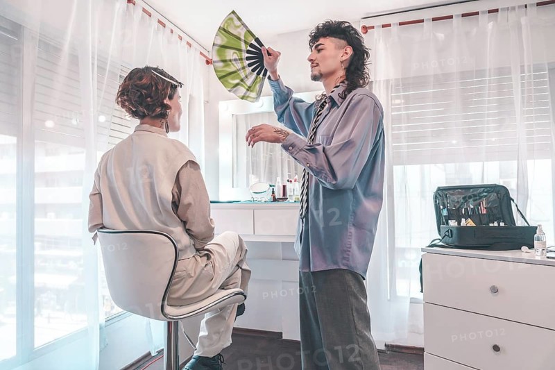 Professional makeup artist using a hand fan to cool a client after applying makeup, demonstrating personalized care and attention in a bright beauty salon environment