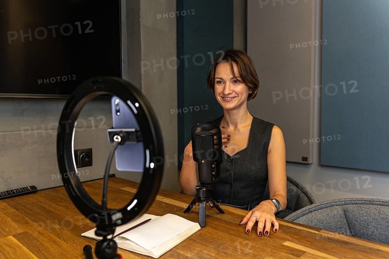 Smiling female content creator gesturing during video recording with professional setup
