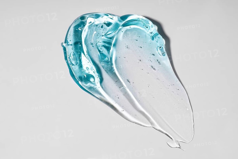 A close-up image of a translucent blue gel texture on a plain, light background. The smooth, flowing pattern highlights the unique, glossy appearance and delicate bubbles