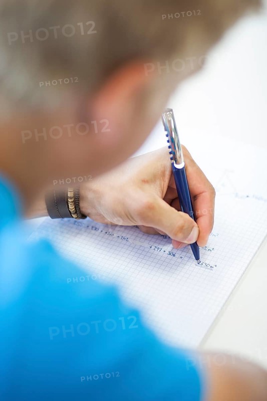 Students write mathematical calculations and area formulas in a checkered notebook with a ballpoint pen, focusing on hands and school assignments