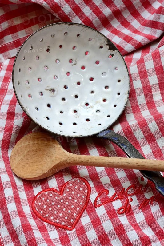 Dish drainer and cooking spoon on kitchen towel with lettering 'Cucina di mamma'