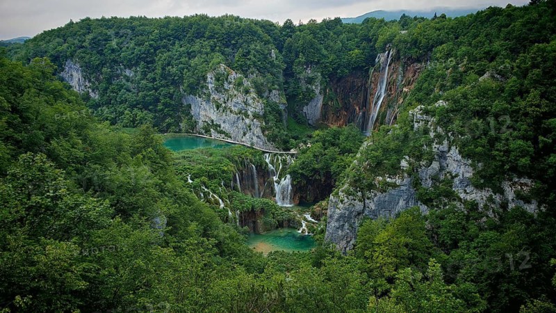 A dramatic waterfall flows through a dense green forest nestled in rock formations, Plitvice Lakes National Park, Croatia