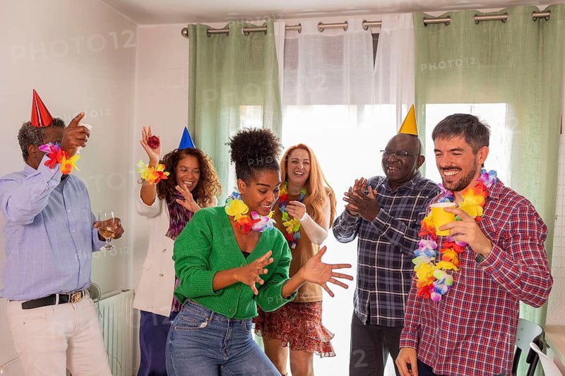 A lively birthday party scene featuring a group of friends dancing and celebrating together. They wear colorful party hats and leis, highlighting joyful togetherness
