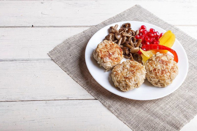 Meatballs with rice mushrooms, sweet peppers and pomegranate seeds on white wooden background. close up