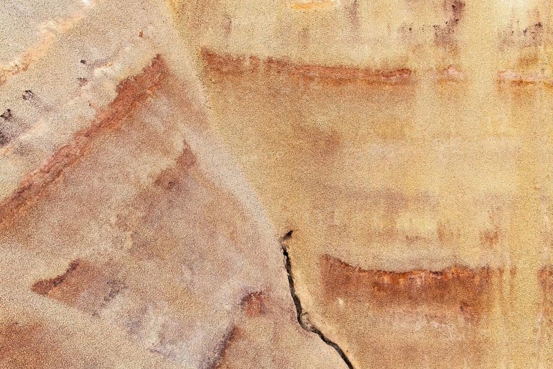 Close up of a multicolored sandstone surface displaying a range of earthy tones with intricate natural patterns and textures. The organic design showcases a crack and multicolored layers