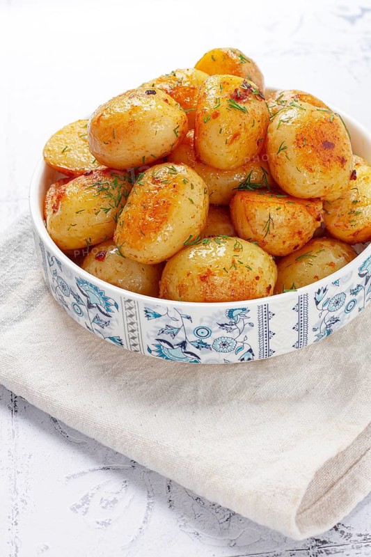 Baked new potatoes, with butter and dill, on a white plate, at home, no people