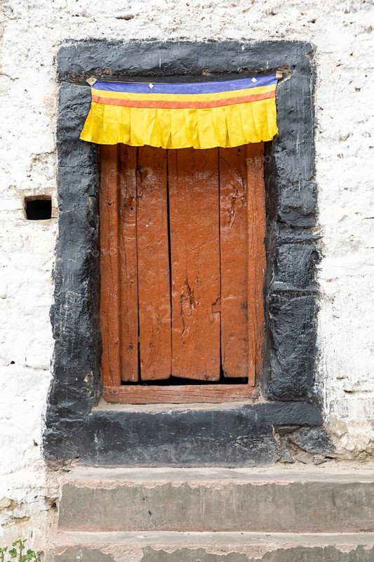 A rustic wooden door adorned with a vibrant yellow, red, and blue fabric in the Zanskar Valley, Ladakh, India, showcasing traditional Himalayan architecture