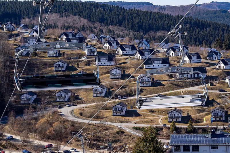 Winter sports area in the Sauerland, Winterberg ski lift carousel, artificial snow slopes, artificial snow from over 360 snow guns, Büre-Herrloh ski area, 12 of 24 lifts are in operation in mid-March, the rest of the landscape is snow-free, in the background holiday homes at Landal Ferienpark Winterberg, North Rhine-Westphalia, Germany