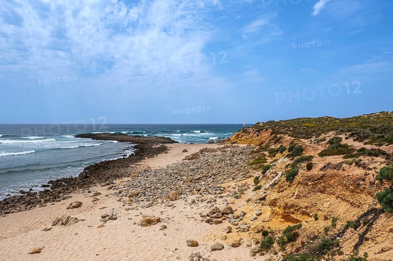 Quiet beach with rocks surrounded by blue skies and gentle ocean waves, Vila Nova de Milfontes, Beja, Portugal