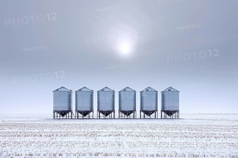 Row of grain bins, stainless steel silos for bulk storage in snow covered field at Saskatchewan in winter, Canada