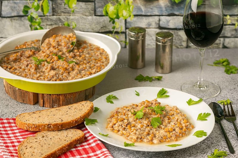 Lentils with bacon in a bowl and on a plate with bread and wine glass