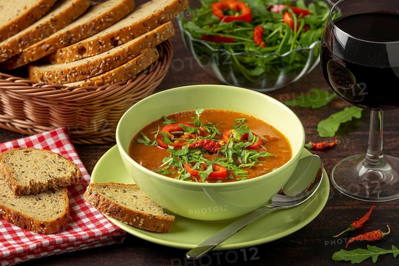 Goulash decorated with paprika and arugula, served with bread, salad and red wine