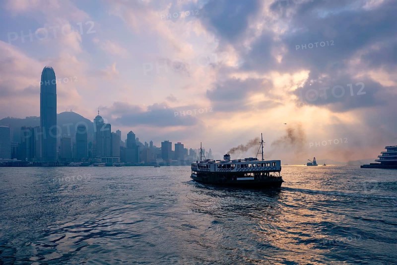 Hong Kong skyline cityscape downtown skyscrapers over Victoria Harbour on sunset with tourist ferry boat silhouette. Hong Kong, China