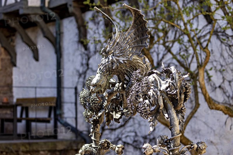 Metal sculpture of a dragon with detailed wings in front of a wall covered with vines, The fountain at Wartburg Castle near Eisenach in Thuringia