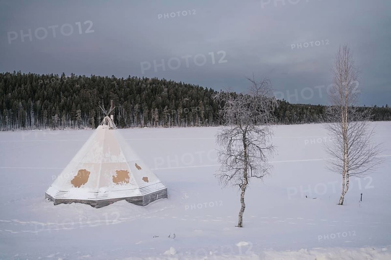 A traditional tipi stands in the snowy expanse of Swedish Lapland, with frosted trees and a dense forest in the background, under a serene winter sky