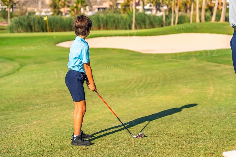 Rear view of a boy focus about to swinging golf in a green luxury course