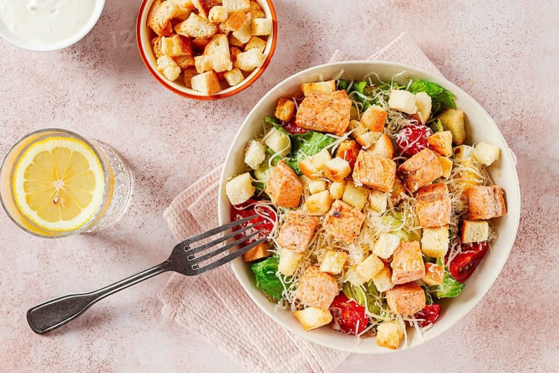 Caesar salad with salmon, with croutons and dressing, in a salad bowl, on a pink table