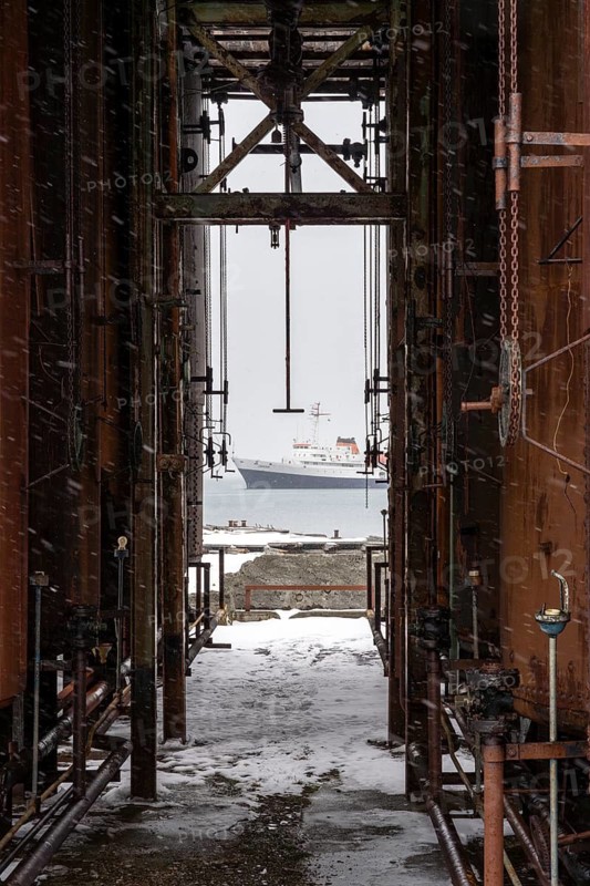 View of the expedition ship Ushuaia in the bay through the rusted industrial plant of the former whaling station, snowfall, Grytviken, South Georgia