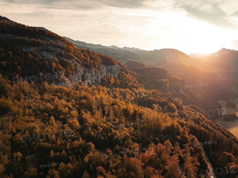 Sunlight floods over a hilly landscape surrounded by an autumnal forest, Meiringen, Switzerland