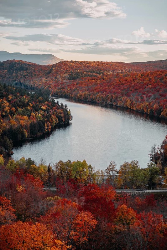 Stunning autumn foliage in Quebec showcases vibrant shades of orange, red, and yellow surrounding a serene river, creating a breathtaking natural panorama under a clear sky