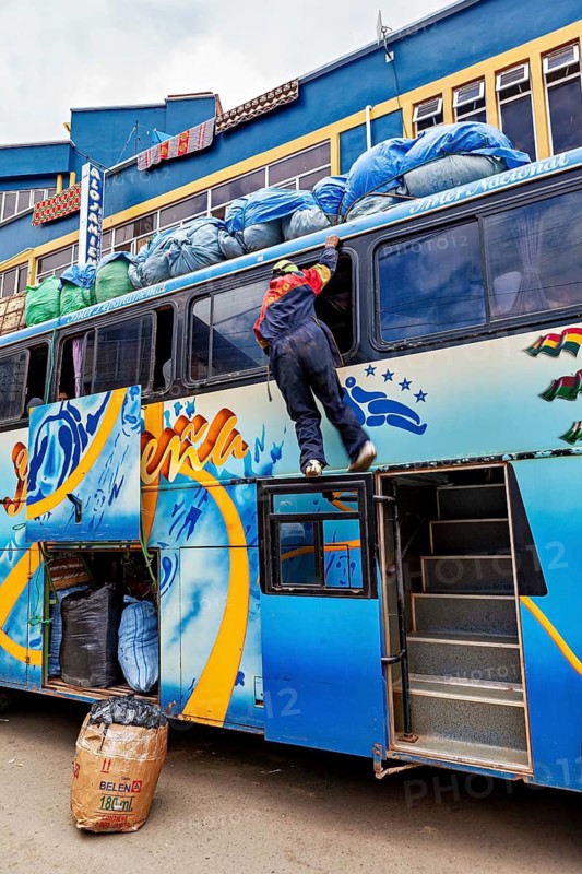 A person climbs onto the roof of a bus to load luggage in an urban setting, bus trip from La Paz to Rurrenabaque via Death Road in Bolivia