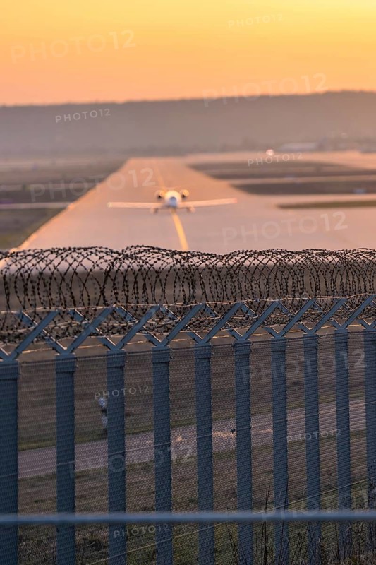 Airplane rolling at airport, barbed wire in foreground, Stuttgart Airport, Germany