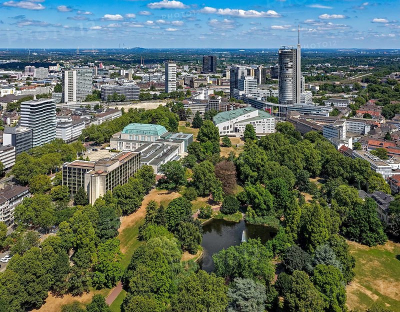 Essen, North Rhine-Westphalia, Germany - City panorama of Essen, skyline with front city garden with lake and fountain, on the left the Sheraton Essen Hotel and the Philharmonic, in the back the Aalto Theatre and the Evonik Tower skyscrapers, former RWE Tower, the Post Bank and at the very back the town hall. Stadtgarten Essen is Essen's oldest publicly accessible green space. It is located south of Essen Central Station in the Südviertel district, between the Aalto Theatre, the Philharmonic and the neighboring Rüttenscheid district. Parks and gardens in the Ruhr area