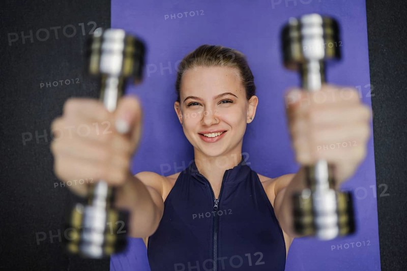 Blonde woman exercising with dumbbells, smiling and confident on a purple yoga mat. A perfect depiction of a healthy lifestyle, strength, and determination in fitness