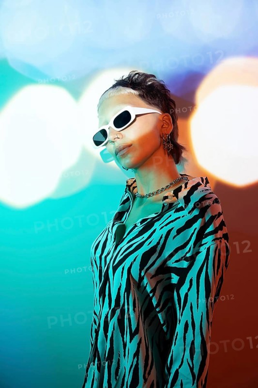 A young, trendy woman exudes confidence in a zebra print top and edgy sunglasses. The vibrant background enhances her modern, bold aesthetic and individuality