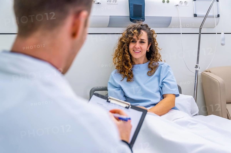 Rear view of an unrecognizable doctor attending female patient on hospital bed