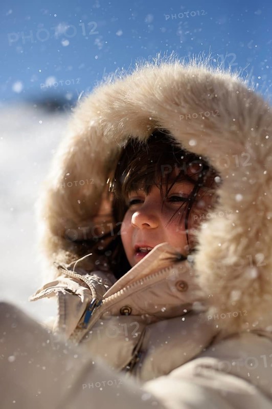 A child enjoys a snowy day at Sierra Nevada Ski Resort in Granada, bundled up in a fluffy hooded coat. The crisp air and falling snow create a magical winter atmosphere