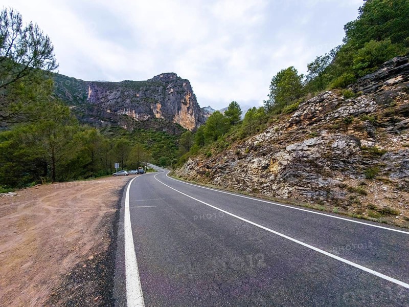 Entremon gorge road curves along the cinca river in huesca, spain, offering a scenic route through the rugged pyrenees mountain landscape with steep rock walls and green trees under a cloudy sky