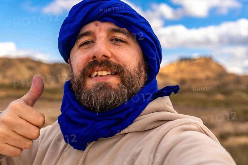 Bearded man wearing blue turban making thumbs up gesture while visiting bardenas reales desert in navarre, spain