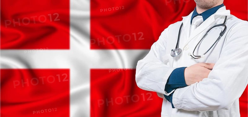 Denmark health care concept. Male doctor on Denmark flag. Doctor with crossed arms on Denmark flag