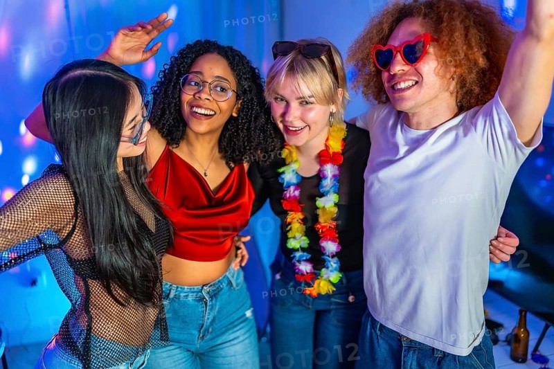 Four cheerful multi ethnic friends are dancing and having fun at a party with blue disco lights