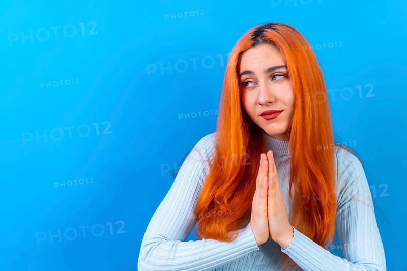 Redhead woman in studio photography making the gesture please on a blue background