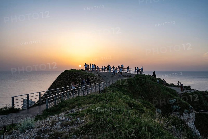 Tourists stand on the observation deck of the Falaise d'Aval rock formation and tourist attraction near Étretat and watch the sunset over the English Channel, Alabaster Coast, La Côte d'Albâtre, Chalk Cliffs, Seine-Maritime, Normandy, France
