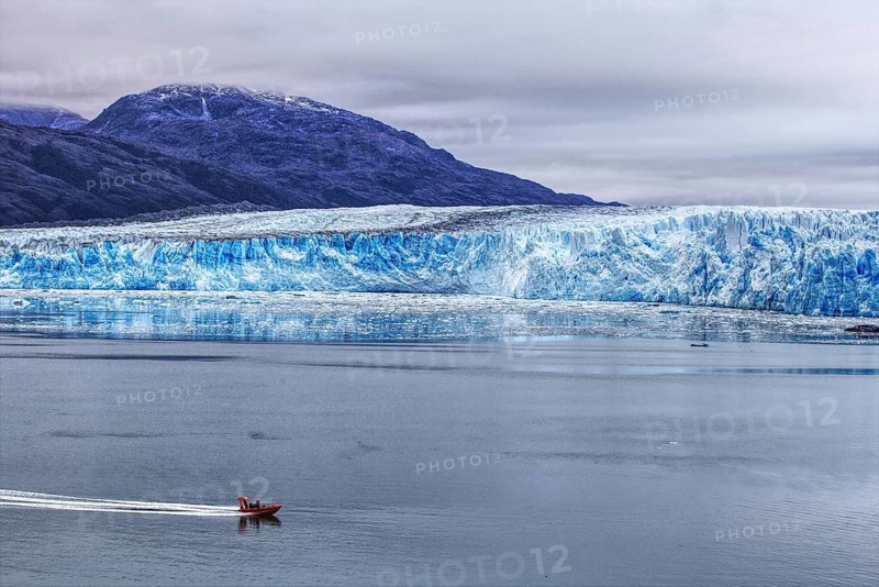 A small boat sails along the impressive Bruges Glacier, which stretches along the edge of the ocean, Chile