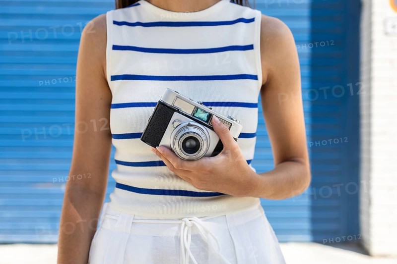 A woman enjoys city life holding a vintage camera, embracing the freedom and creativity of outdoor photography. Her striped top complements the urban backdrop
