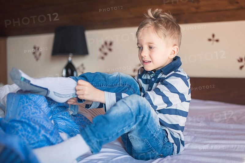 Five years old boy dresses his socks in the morning on the bed